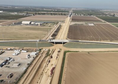Aerial view of concrete overpass above an unpaved road. The overpass is surrounded by agricultural land that has been cleared and is brown in color.